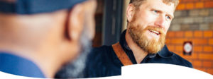 A bearded man stands talking to another man.