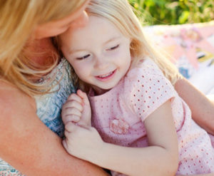 A woman sits outside with her smiling daughter in her arms.