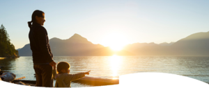 A small child stands on the shore and points into the distance accompanied by his mother holding his hand at sunset.
