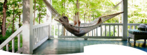 A woman lays reading in a knit hammock hanging beneath her fenced-in porch.