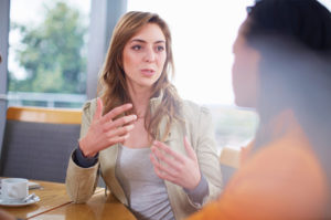 A woman eagerly talks to another woman across the table from her.