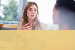 A woman eagerly talks to another woman across the table from her.