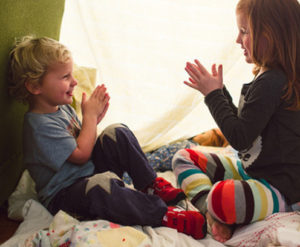 Two small children play under a blanket fort.